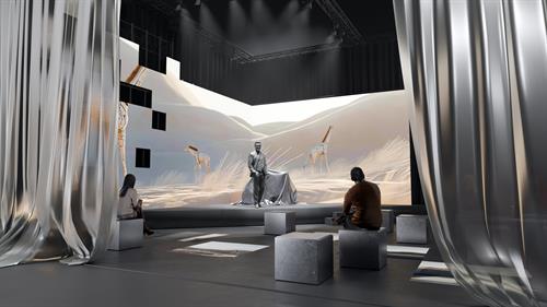 Eine Bühneninstallation mit geschwungenen LED-Wänden zeigt eine stilisierte Wüstenlandschaft mit Giraffen. In der Mitte steht eine Person neben einem verhüllten Objekt. Einige Besucher*innen sitzen auf würfelförmigen Hockern im abgedunkelten Raum mit seitlich drapierten Vorhängen.